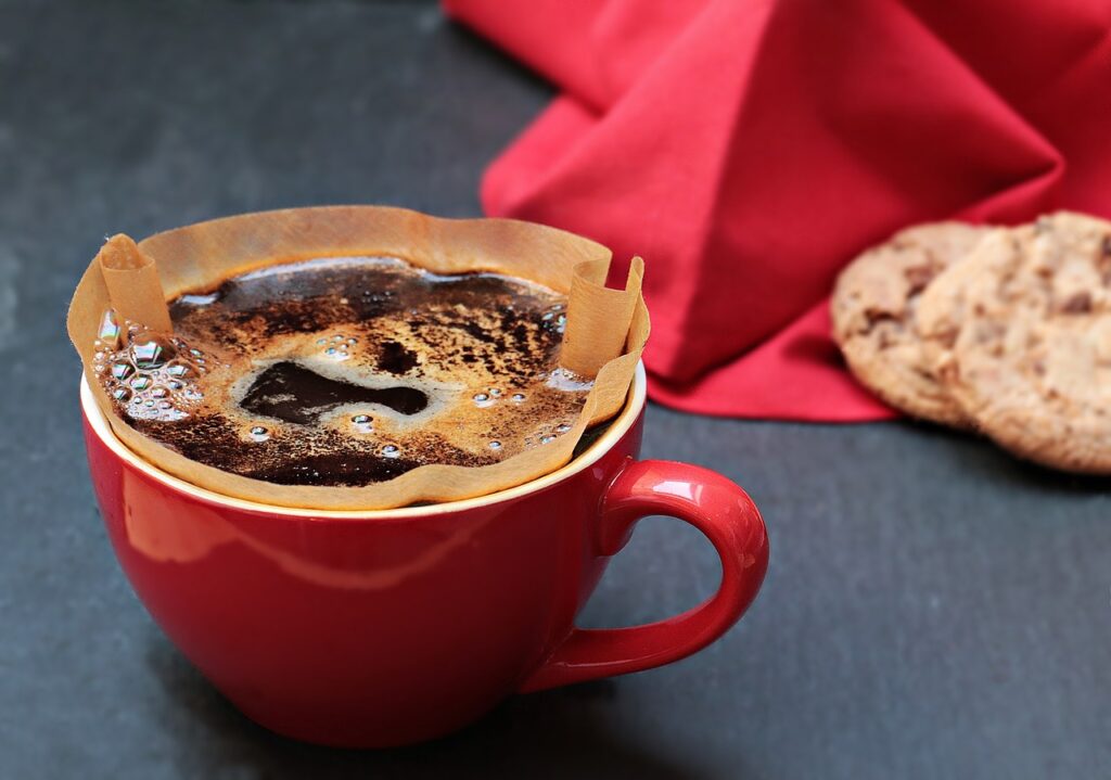 xícara vermelha com café e dois biscoitos de fundo em cima de um pano vermelho