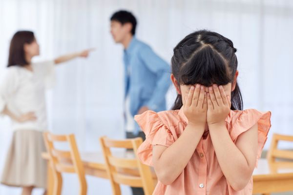 magoa dos pais homem e mulher brigando no fundo da foto e uma criança com a mão no rosto chorando