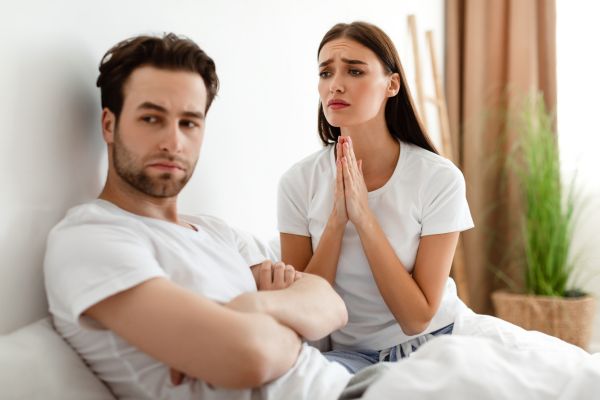 como lidar com a insegurança no relacionamento amoroso um homem sentado com uma mulher olhando pra ele angustiada e ele de braços cruzados