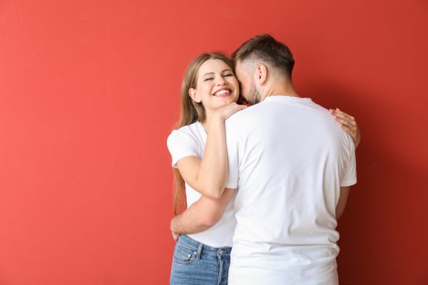 relacionamento afetivo duradouro uma jovem mulher abraçada em pé a um jovem homem com fundo vermelho