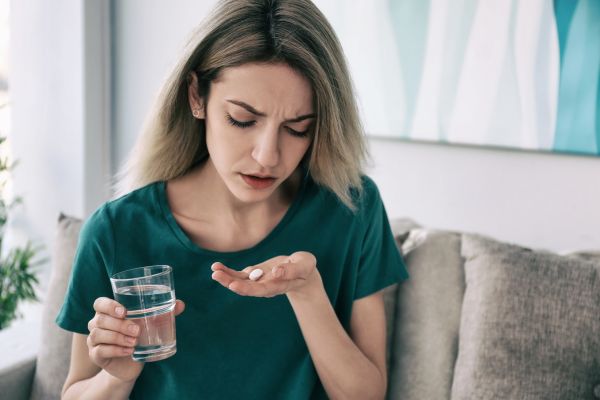 antidepressivo mulher sentada no sofá com copo de agua e pilula na mão pra tomar