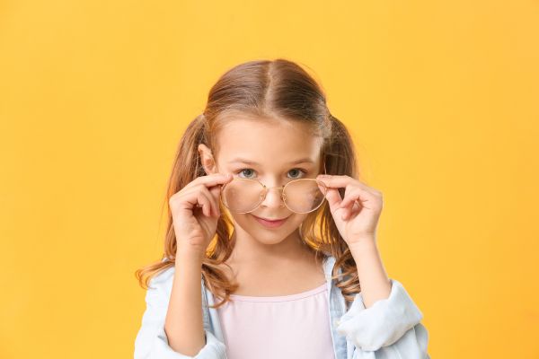 uma criança, menina, com mãos nos óculos tirando do rosto