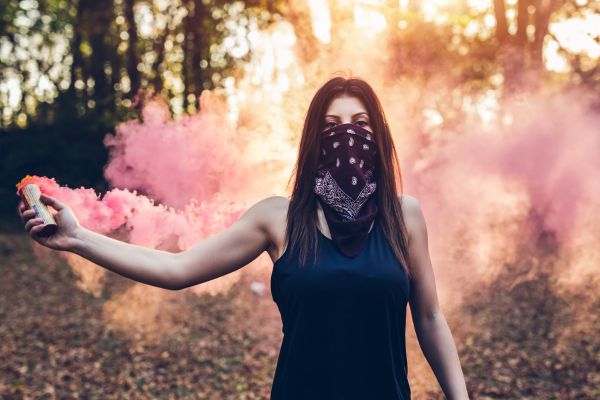 mulher com lenço no rosto soltando fumaça rosa