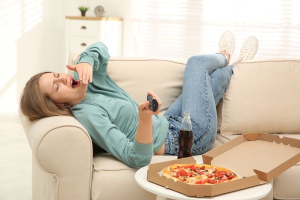 sabotadores mentais mulher deitada comendo pizza com coca cola bocejando