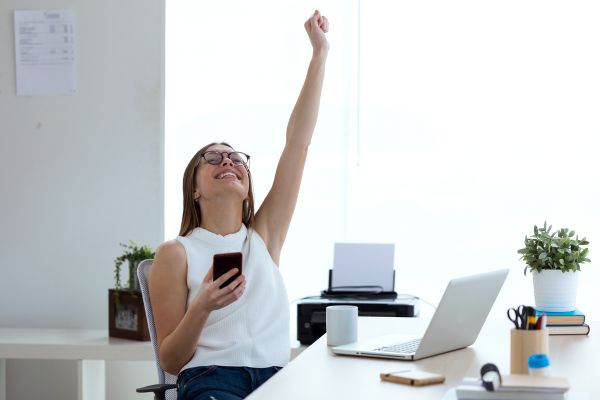 como ter sucesso na vida profissional mulher levantando o braço comemorando com computador e celular na mão