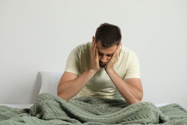 o que é carencia afetiva homem com mãos no rosto sentado na cama com cobertor