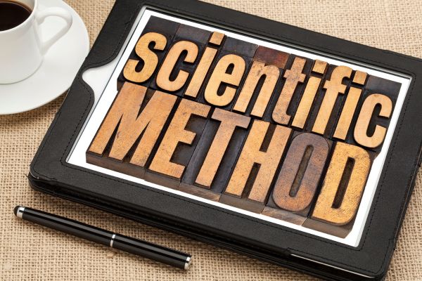caneta, café e caderno escrito método cientifico em inglês