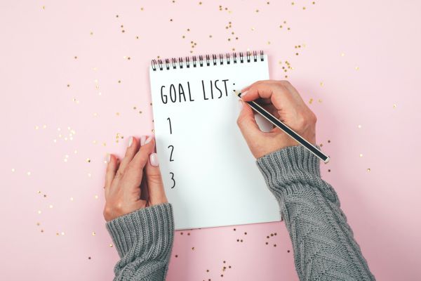 acompanhar-progresso-metas-de-forma-objetiva Pessoa anotando uma lista de metas em um caderno, representando o acompanhamento do progresso de forma objetiva