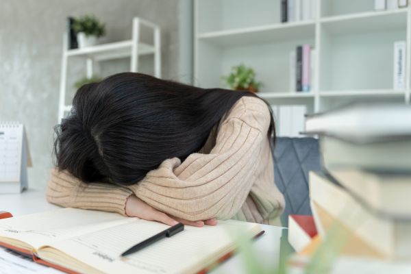 quando tiver desanimado mulher apoiando a cabeça nos cadernos representando desânimo