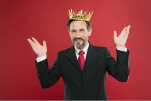 fundo vermelho com homem de terno preto, gravata vermelha, com corroa de rei na cabeça e braços levantados