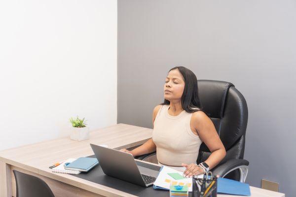 mulher sentada no escritório coom olhos fechados representando mindfulness