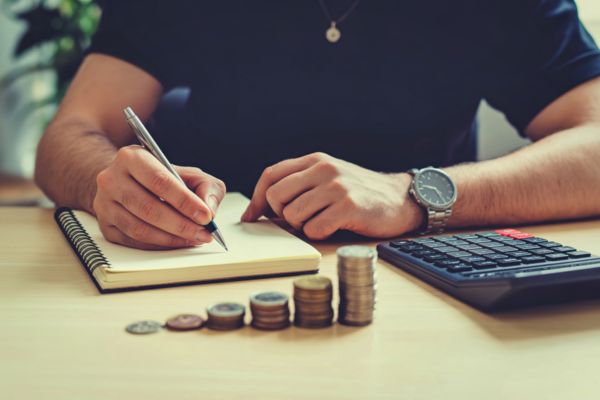 Homem organizando finanças após separação, escrevendo em caderno com calculadora e moedas sobre a mesa.