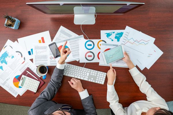 a analise swot duas pessoas com teclado de computador e vários papeis representando uma analise swot