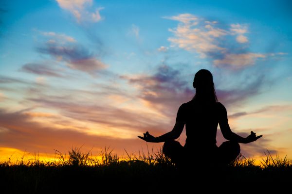 meditação e autoconhecimento mulher meditando com o por do sol no fundo e ceu azul