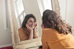 Mulher sorrindo para o próprio reflexo no espelho representando autoestima e identidade fortalecida