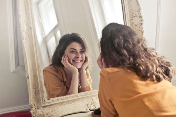 Mulher sorrindo para o próprio reflexo no espelho representando autoestima e identidade fortalecida