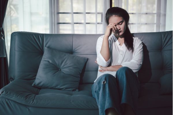 causas da depressão isolamento emocional Pessoa sentada no sofá com expressão de cansaço emocional, ilustrando fatores emocionais associados às causas da depressão