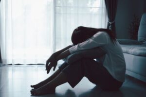 Pessoa sentada no chão em ambiente interno, demonstrando isolamento e tristeza associados à depressão