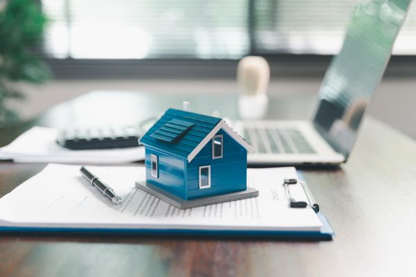 Miniatura de casa sobre documentos financeiros simbolizando investimento imobiliário e construção de patrimônio.