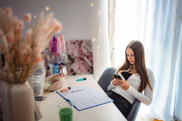 produtividade procrastinacao distração celular jovem usando celular enquanto agenda de estudos está aberta na mesa representando procrastinação e falta de foco