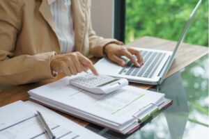 Pessoa analisando documentos financeiros e usando calculadora e notebook para planejamento de investimentos e construção de patrimônio