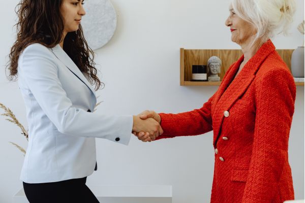 quando buscar ajuda vida proposito Duas mulheres apertando as mãos em ambiente profissional representando busca de ajuda para redefinir vida e propósito.