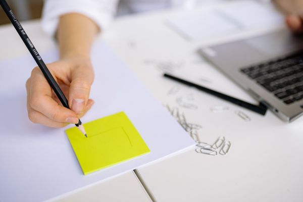 como aplicar reconexão com identidade no cotidiano Pessoa escrevendo em um papel ao lado do computador, representando planejamento e aplicação prática de mudanças na vida cotidiana.
