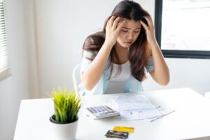 Mulher preocupada analisando contas e cartão de crédito representando erros financeiros e dificuldades com finanças pessoais.