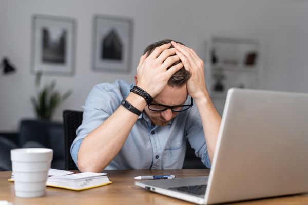 erros que destroem independencia financeira Homem estressado diante do computador representando erros financeiros que impedem a independência financeira
