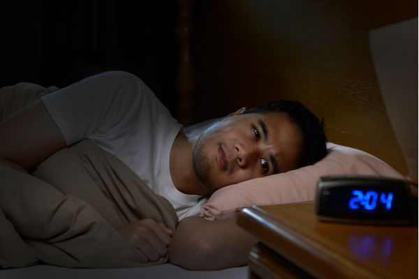 fadiga mental sono fragmentado noite Homem acordado na cama à noite olhando para o relógio devido à fadiga mental e dificuldade para dormir