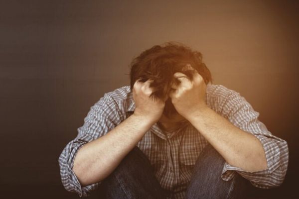baixa auto estima autosabotagem emocional Homem com a cabeça entre as mãos demonstrando frustração, baixa autoestima e sofrimento emocional