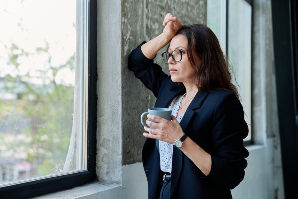 impacto da autosabotagem cansaço emocional Mulher pensativa e cansada olhando pela janela com expressão de preocupação e desgaste emocional