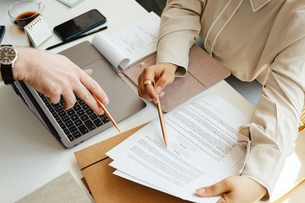 Pessoas analisando documentos e um notebook, representando como escolher a melhor agenda digital para organizar a rotina.